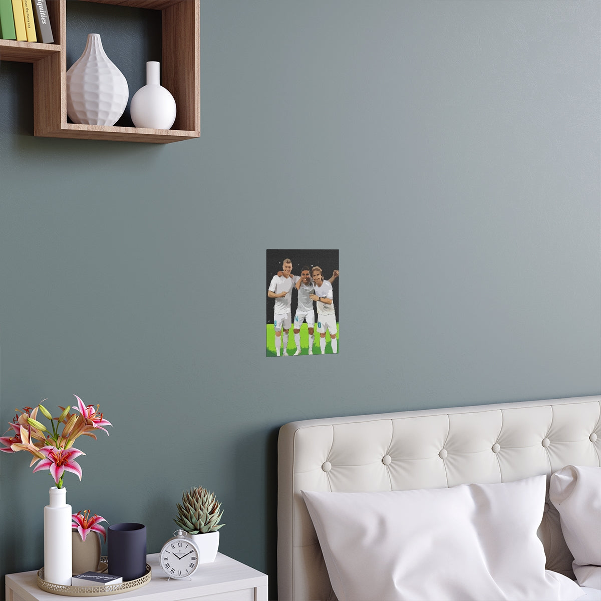 Contextual Front view of Toni Kroos, Casemiro and Luka Modric arm in arm on a black poster hanging on a wall above a double bed.