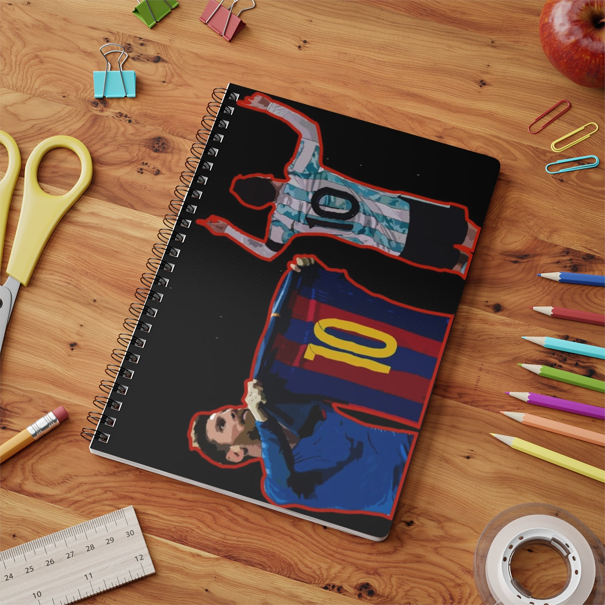 Contextual Front view of Barcelona and Argentina Lionel Messi iconic celebrations against black background A5 spiral notepad on a table top.