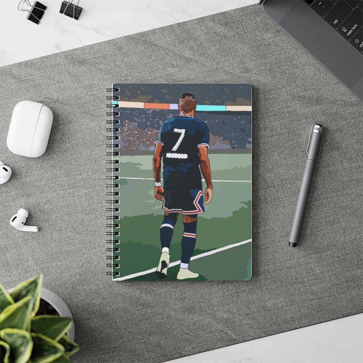 Contextual Front view of PSG Mbappe on football pitch A5 spiral notepad on desk top.