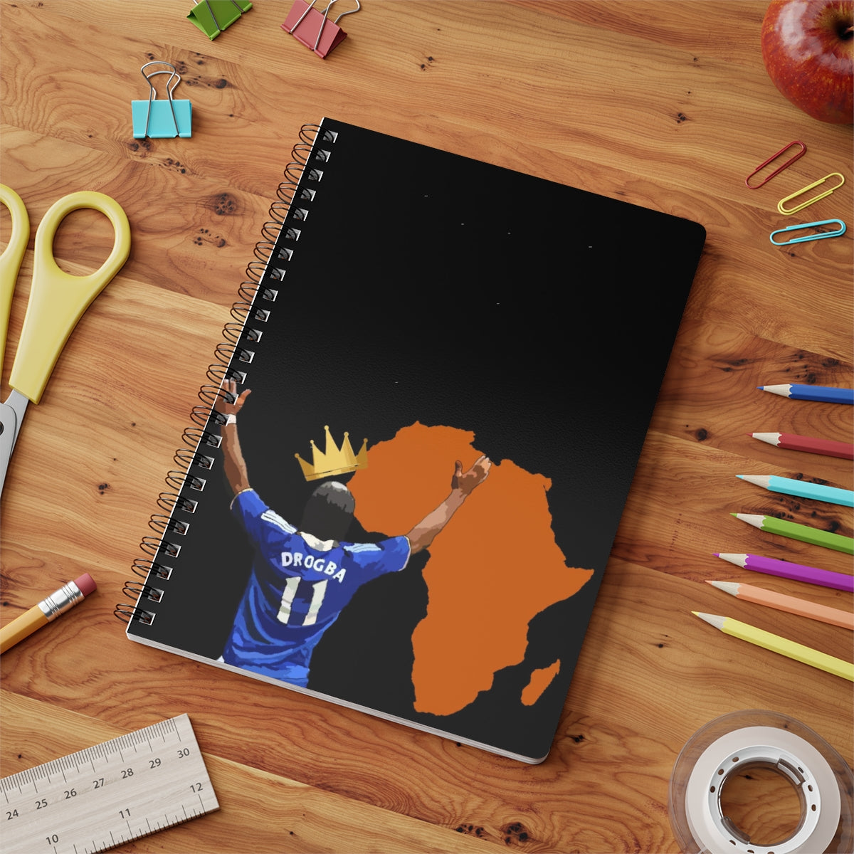 Contextual Front view of Chelsea Didier Drogba with a crown a top his head with the orange coloured continent of Africa on an A5 spiral notepad on a desk top.