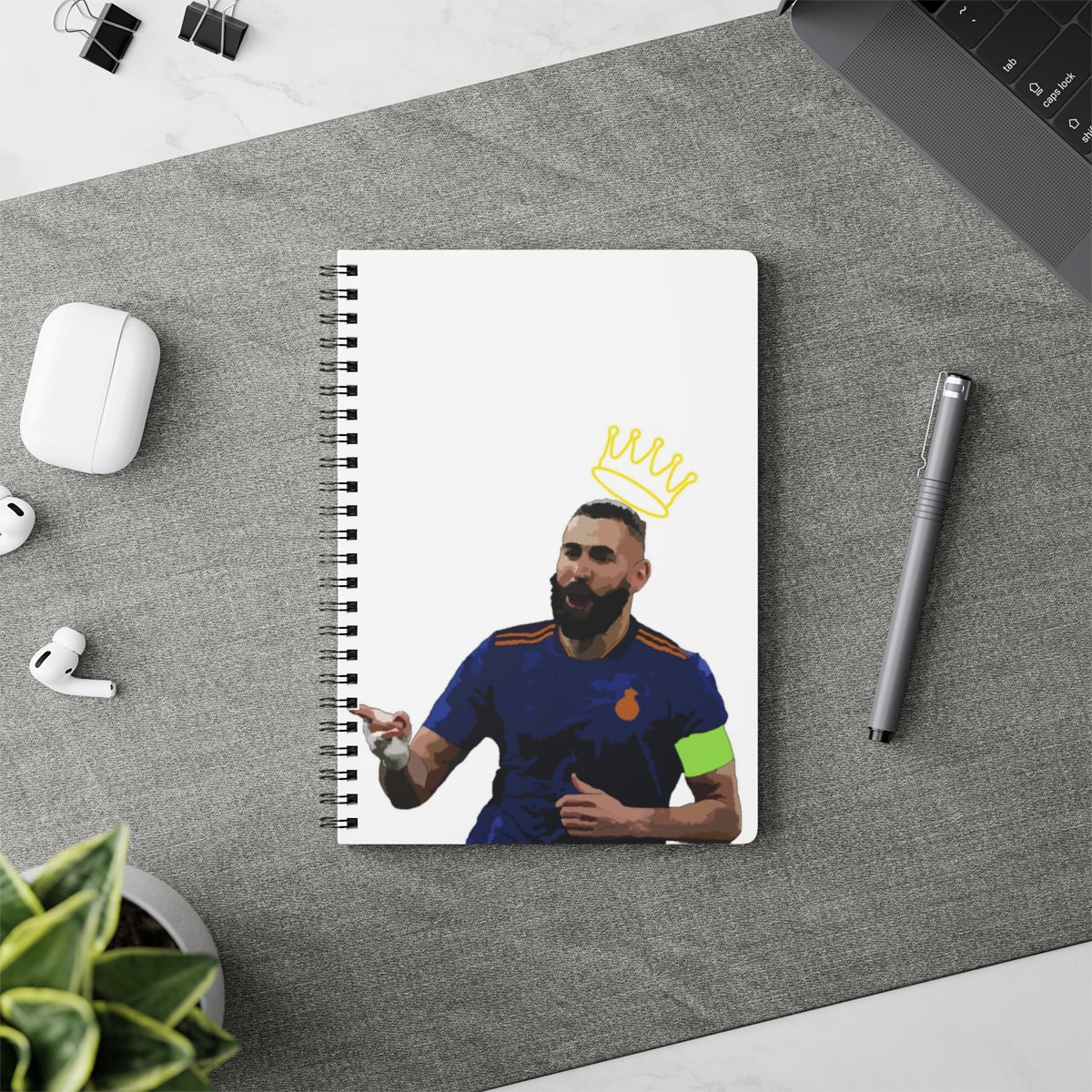 Contextual Front view of Karim Benzema Madrid with crown a top his head against white background A5 spiral notepad on desk top.